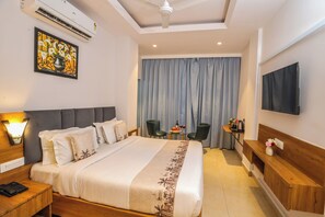 A hotel room with a bed, a desk, a chair, a television, and a window with curtains. - Hotel JHD Luxury Stay Restro & Sky Bar (Udaipur)