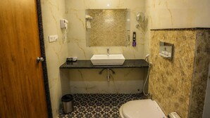 A bathroom with a marble sink, a toilet, a shower, and a trash can. - Hotel JHD Luxury Stay Restro & Sky Bar (Udaipur)