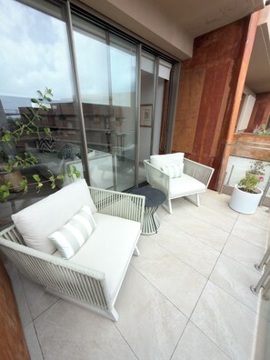 Un balcon agrémenté de meubles en osier blanc, comprenant un canapé et deux fauteuils, ainsi qu’une petite table.