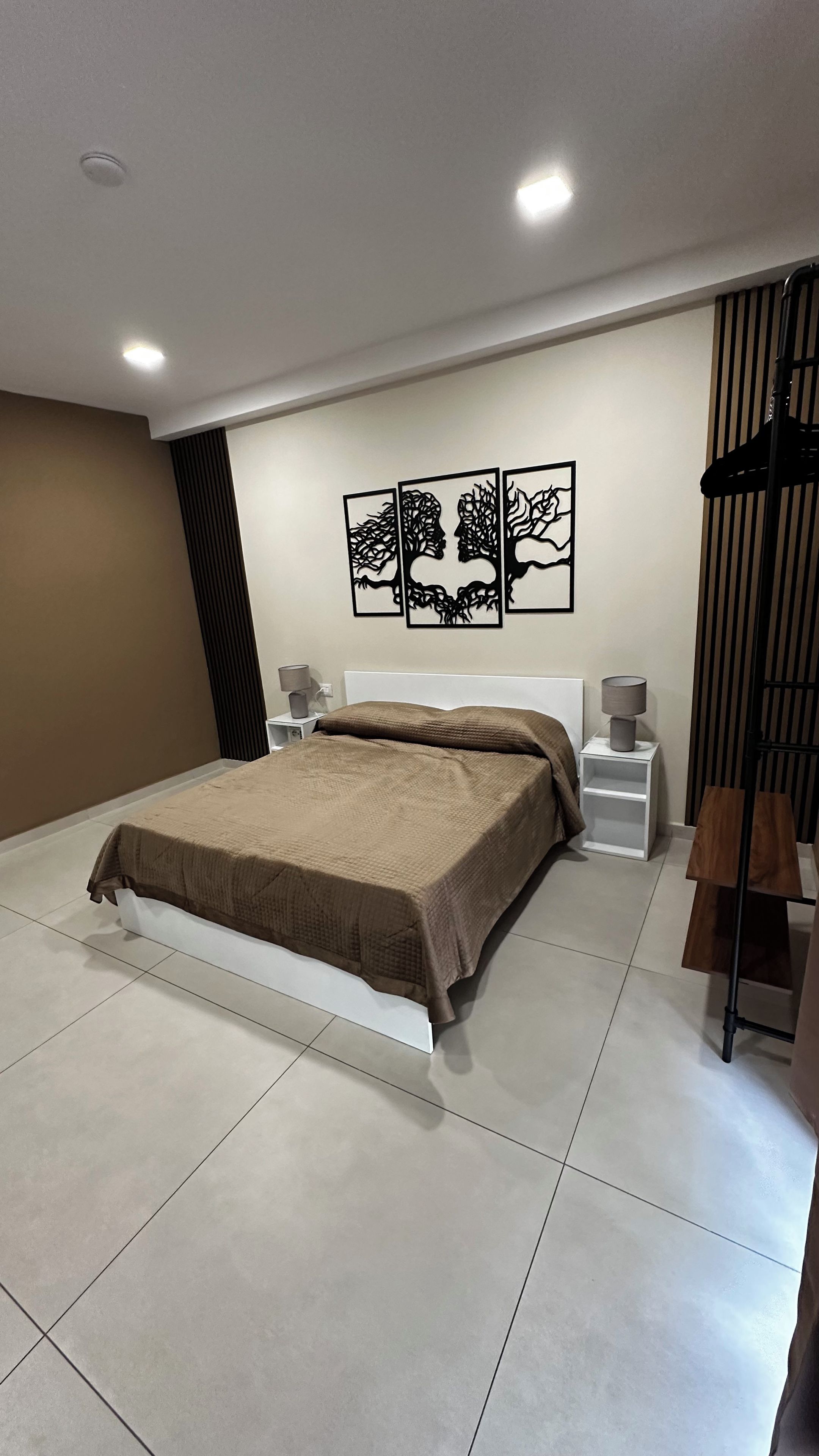 A modern bedroom with a large bed, a nightstand, a lamp, and a wall-mounted artwork.