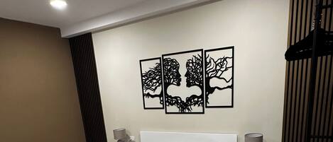 A modern bedroom with a large bed, a nightstand, a lamp, and a wall-mounted artwork.