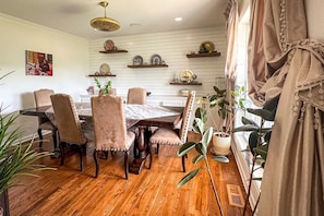 Un comedor con mesa y sillas de madera, estantes decorativos en la pared y plantas en macetas.
