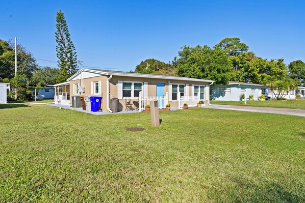 A single-story house with a front porch, a blue trash bin, and a small garden area. - Beautiful Home in Vero Beach, 5 Min to Beach, Sleeps 6, King Bed (Vero Beach)