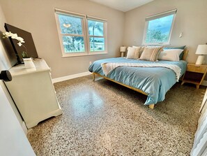 Une chambre à coucher avec un lit, deux fenêtres, une table de chevet, une lampe et un réfrigérateur.