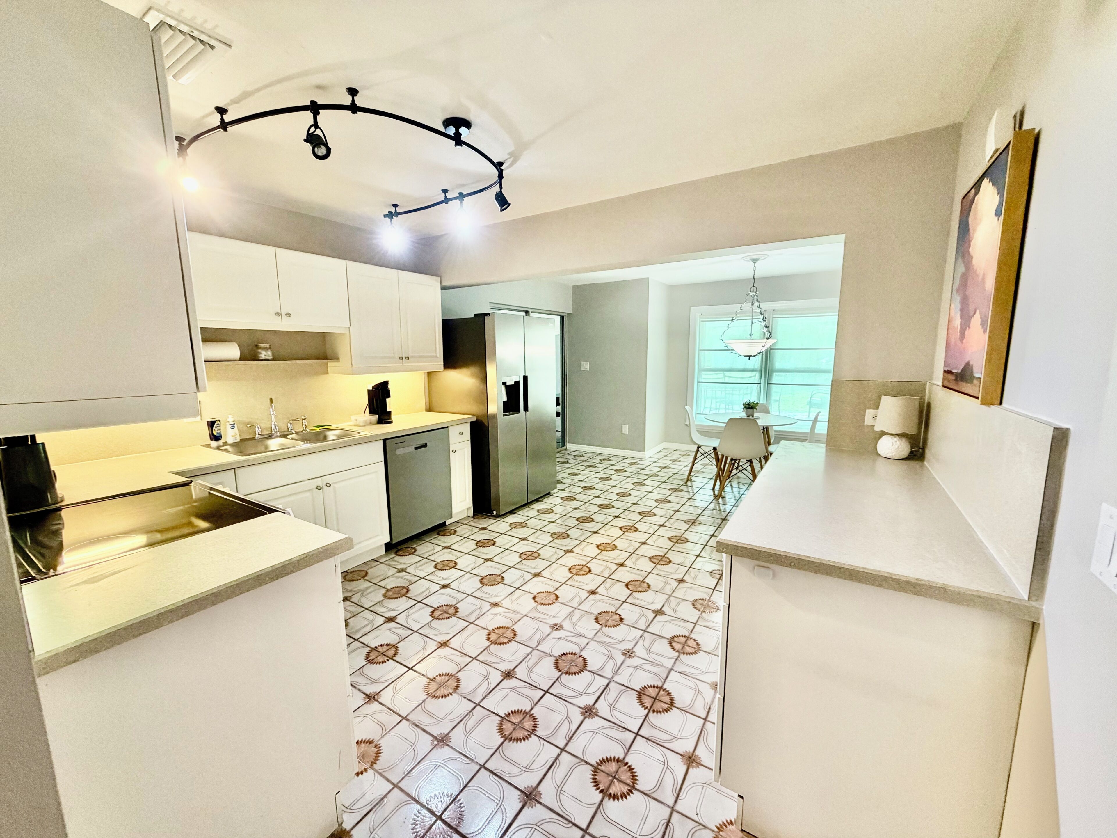 Una cocina moderna con armarios blancos, electrodomésticos de acero inoxidable y baldosas de suelo estampadas.