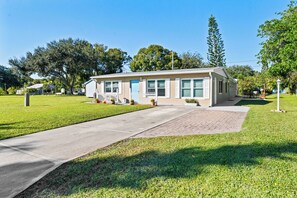 A single-story building with a front porch, a paved driveway, and a well-maintained lawn. - Beautiful Home in Vero Beach, 5 Min to Beach, Sleeps 6, King Bed (Vero Beach)
