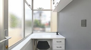 Quarto pequeno com uma escrivaninha branca, uma cadeira e janela com vidro fosco.