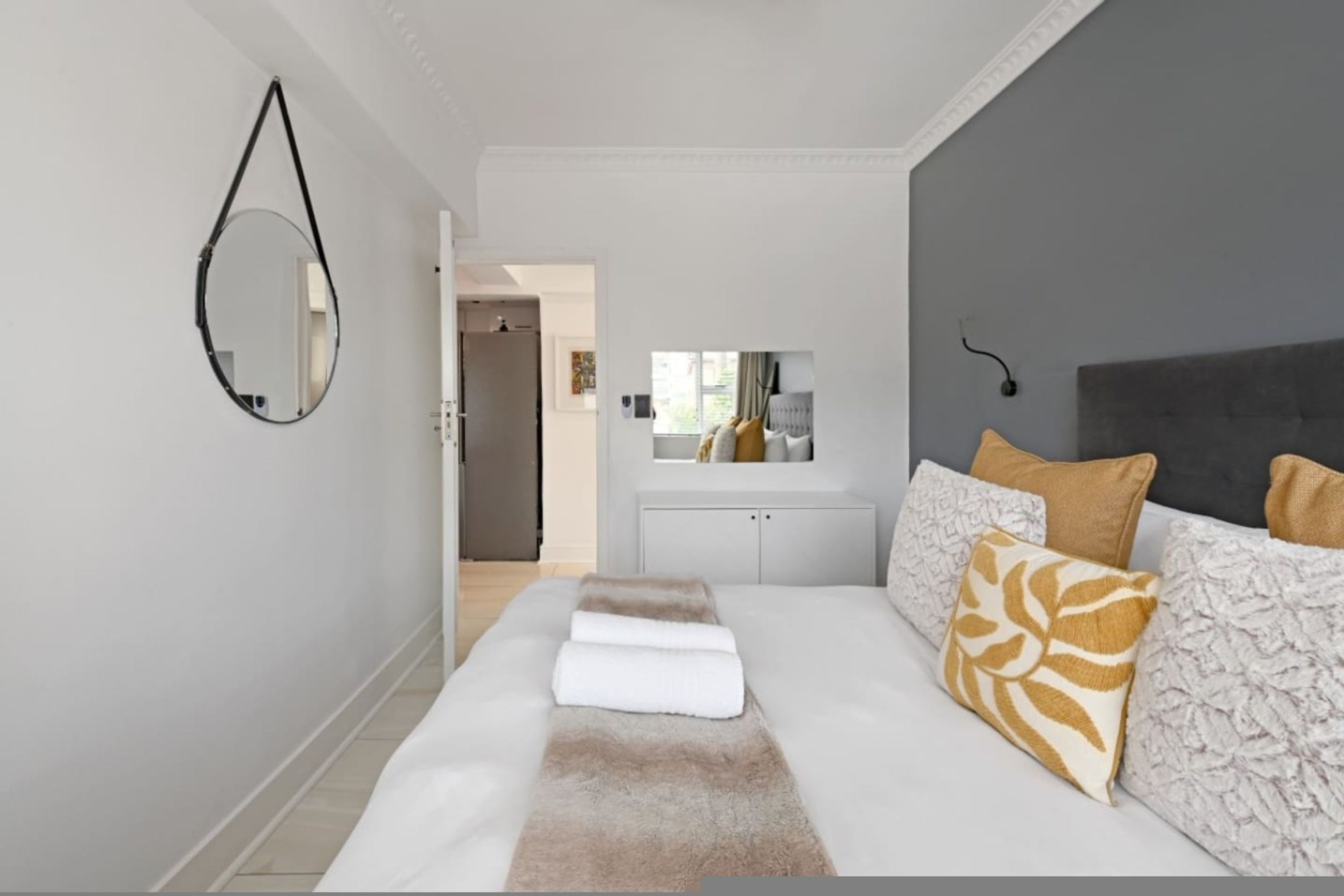 A hotel room with a bed, a mirror, a wardrobe, and a view of the hallway.