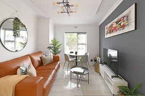 Uma sala de estar moderna com um sofá de couro, um espaço de refeições com cadeiras, uma TV e um grande quadro abstrato na parede.