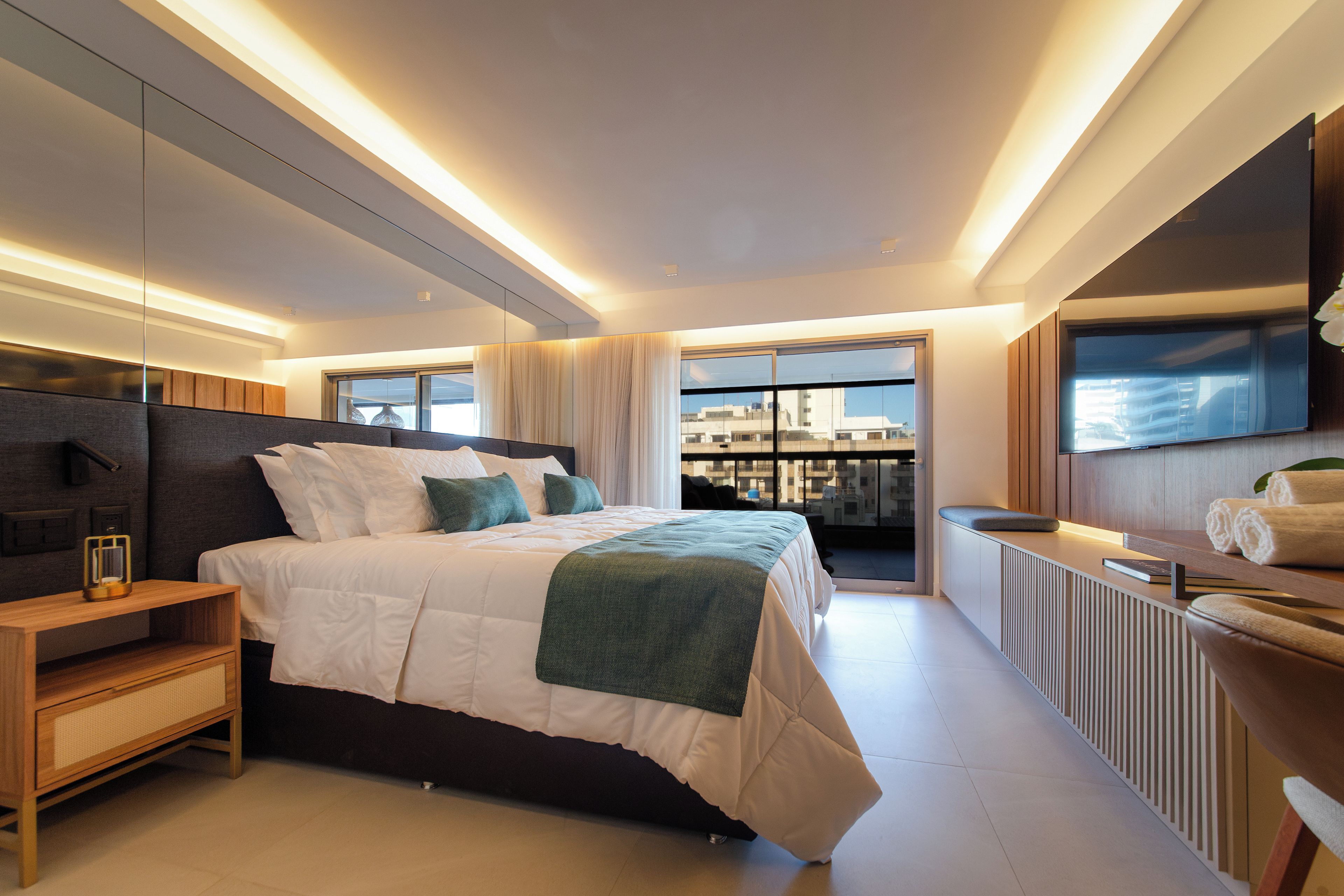 Une chambre moderne avec un grand lit, des tables de chevet, une vue sur la ville et un balcon.