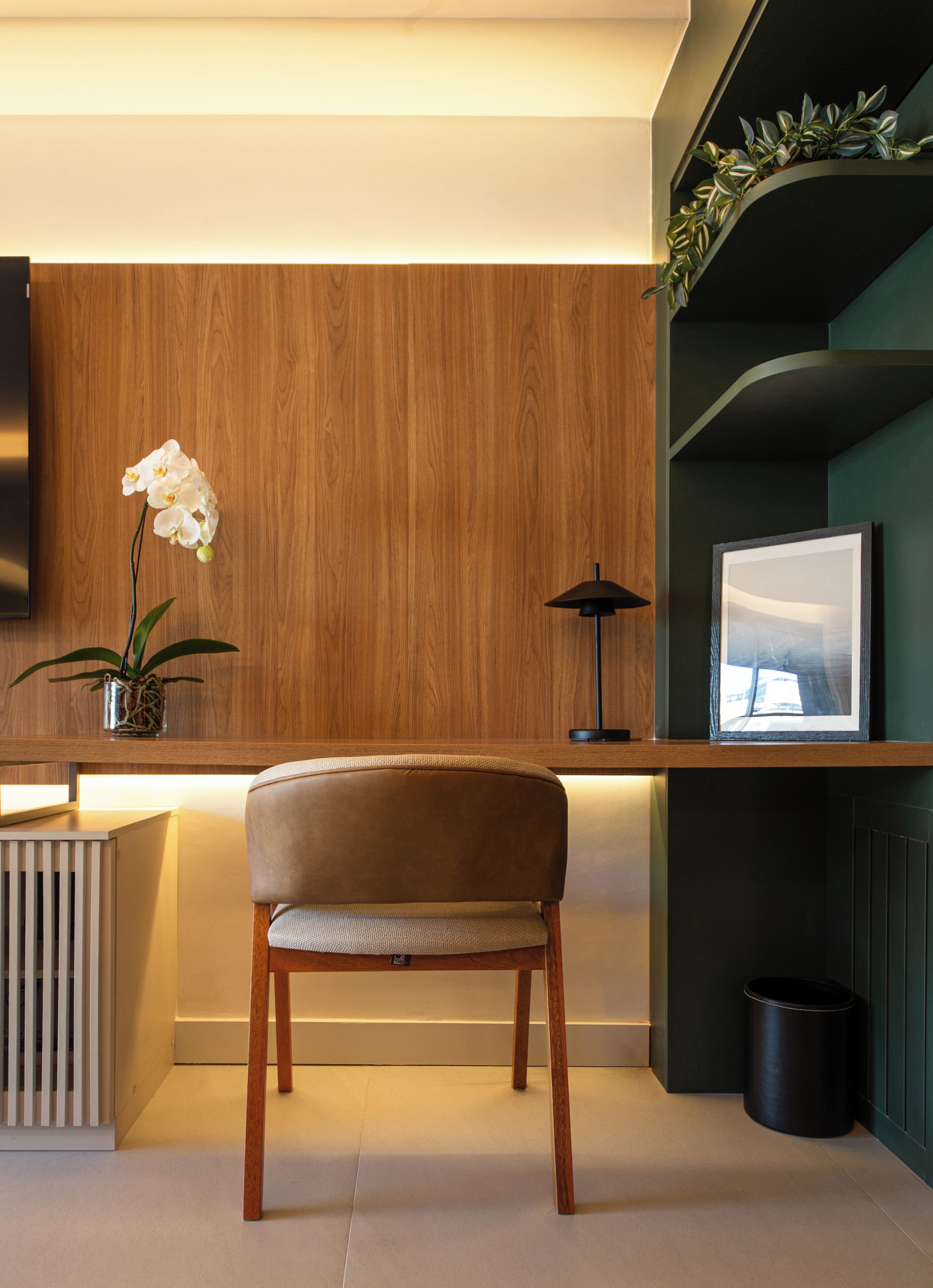 A modern interior with a wooden panel wall, a cushioned chair, a small potted plant, a floor lamp, and a framed picture on a shelf.