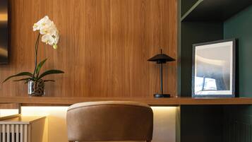 Un interior moderno con un panel de madera, un sillón acolchado, una pequeña planta en maceta, una lámpara de pie y un cuadro en una estantería.