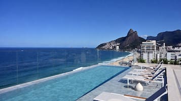 Un ciel d’un bleu éclatant, une piscine avec des chaises longues et une vue sur l’océan et les montagnes.