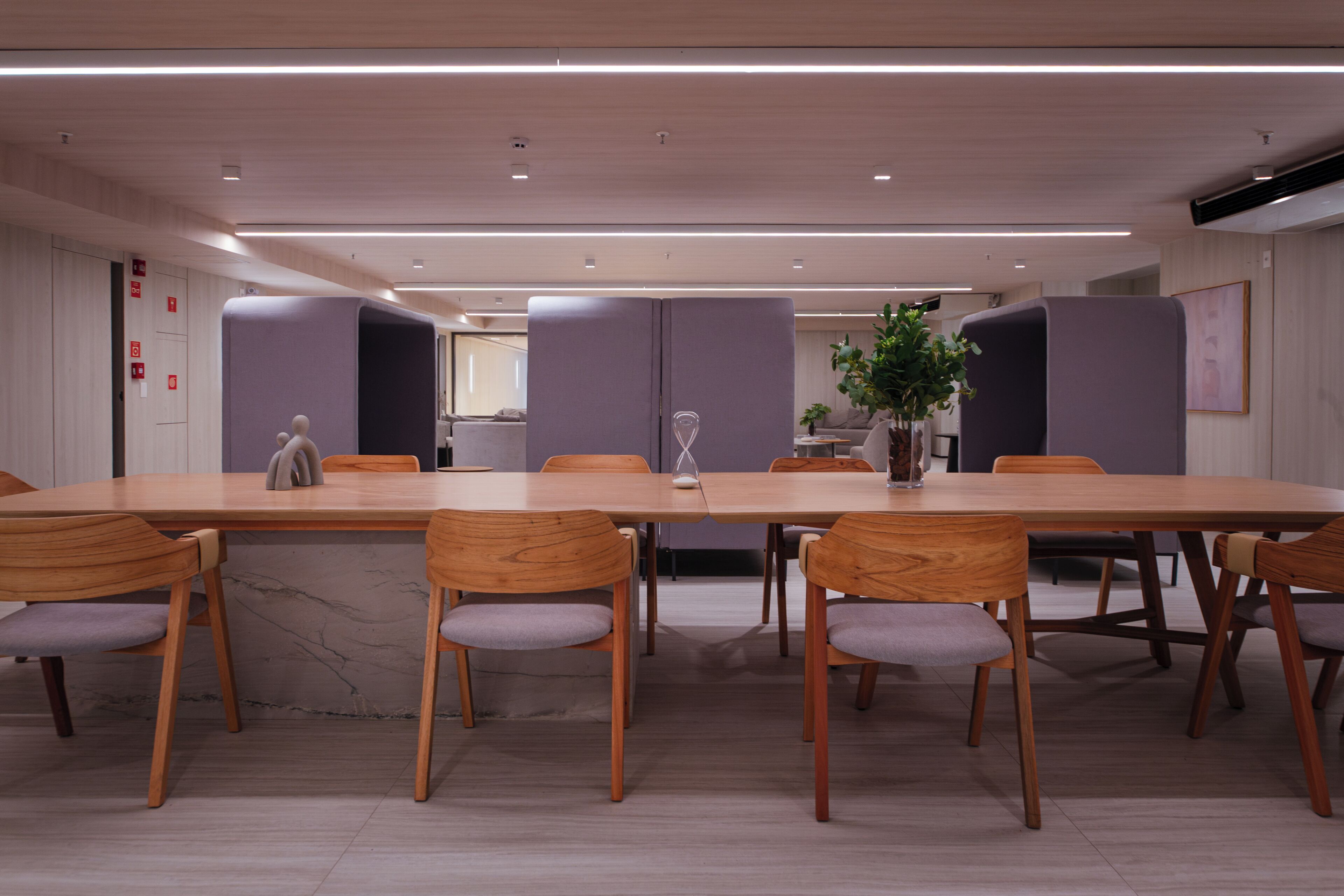 Una sala de conferencias moderna con una larga mesa, sillas de madera y una planta en maceta.