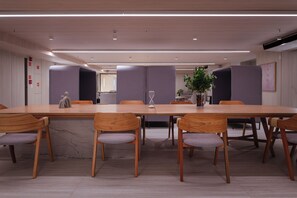 Una sala de conferencias moderna con una larga mesa, sillas de madera y una planta en maceta.