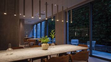 Un espace de salle à manger moderne avec une table en marbre, des chaises en bois, un éclairage suspendu et de grandes fenêtres donnant sur un jardin.