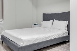 A single-bed room with a grey upholstered headboard, white bedding, and a small bedside table with a tissue box.