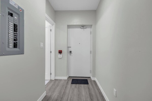 A hallway with a door, a fire alarm, and an electrical panel.