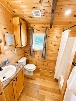 Une petite salle de bain en bois, équipée de toilettes, d’un lavabo et d’un rideau de douche.