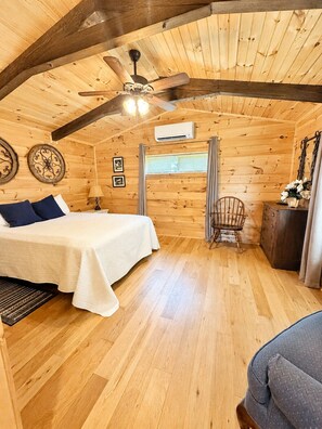 Une chambre confortable, aménagée dans un chalet en bois, avec un lit, une chaise, une commode et un ventilateur de plafond.