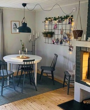 Ein Essbereich mit einem runden Tisch, schwarzen Stühlen, einer hängenden Leuchte, einer Wandverkleidung mit Fotos und Grünpflanzen sowie einem Kamin.