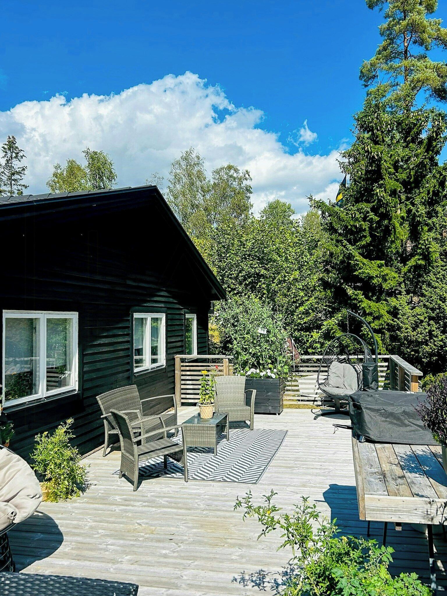 Une terrasse en bois avec des meubles d’extérieur, une petite maison et un paysage boisé en arrière-plan.