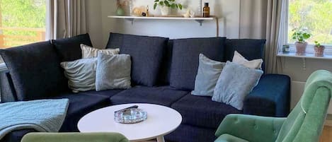 A living room with a dark blue sofa, two green armchairs, a white coffee table, and a bookshelf with various items.
