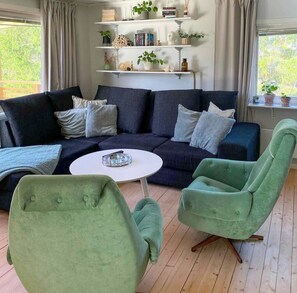 A living room with a dark blue sofa, two green armchairs, a white coffee table, and a bookshelf with various items. - Country retreat on Håtö near sea and fishing (Stockholms län)