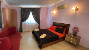 Ein Hotelzimmer mit einem Bett, einem roten Sessel, einem Nachttisch und einer Wand-Klimaanlage.
