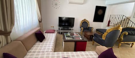 Sala de estar com sofá, televisão, relógio decorativo na parede e escada.