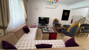 Ein Wohnzimmer mit einer Couch, Fernseher, Wanduhr und einer Treppe.
