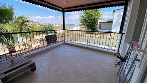 Ein überdachter Balkon mit Fliesenboden, einer hölzernen Bank und einem Metallgeländer.