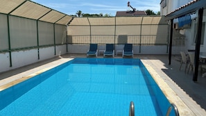 Una piscina con borde de azulejos, rodeada por una zona cubierta con techo y una pared con barandilla de metal.