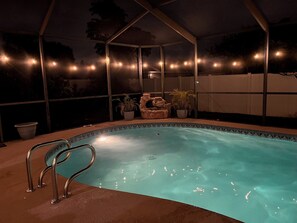 Piscina com escada de metal, rodeada por área coberta com luzes de corda.