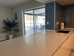 A kitchen with a white countertop, a sink, and a blue backsplash. There is a potted plant on the left and a view of outdoor seating through a glass door. - 3-bedroom family friendly with pool in wonderful Largo just minutes to beaches (Largo)
