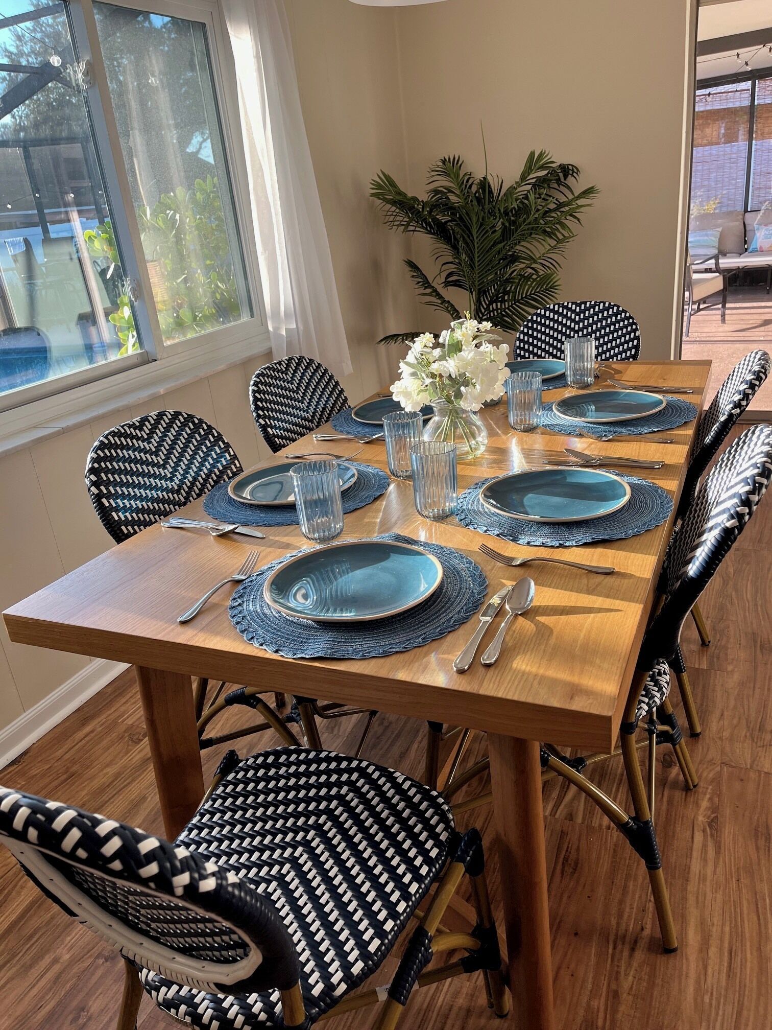 Une table à manger dressée avec de l’argenterie, des assiettes bleues et des verres transparents, entourée de chaises aux motifs noir et blanc.
