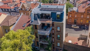 Um edifício de vários andares com terraço no telhado, varandas e vista para a área urbana circundante.