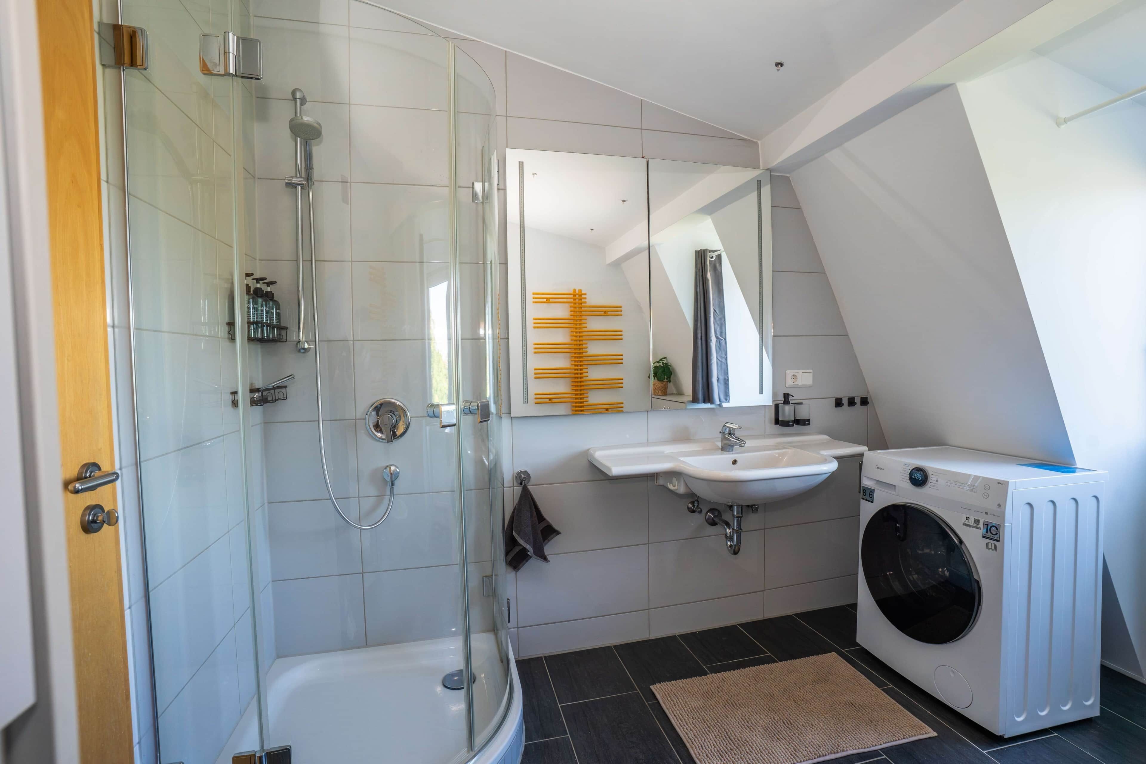 Ein modernes Badezimmer mit Duschkabine aus Glas, integriertem Waschbecken, Waschmaschine und Handtuchhalter.