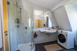 Ein modernes Badezimmer mit Duschkabine aus Glas, integriertem Waschbecken, Waschmaschine und Handtuchhalter.