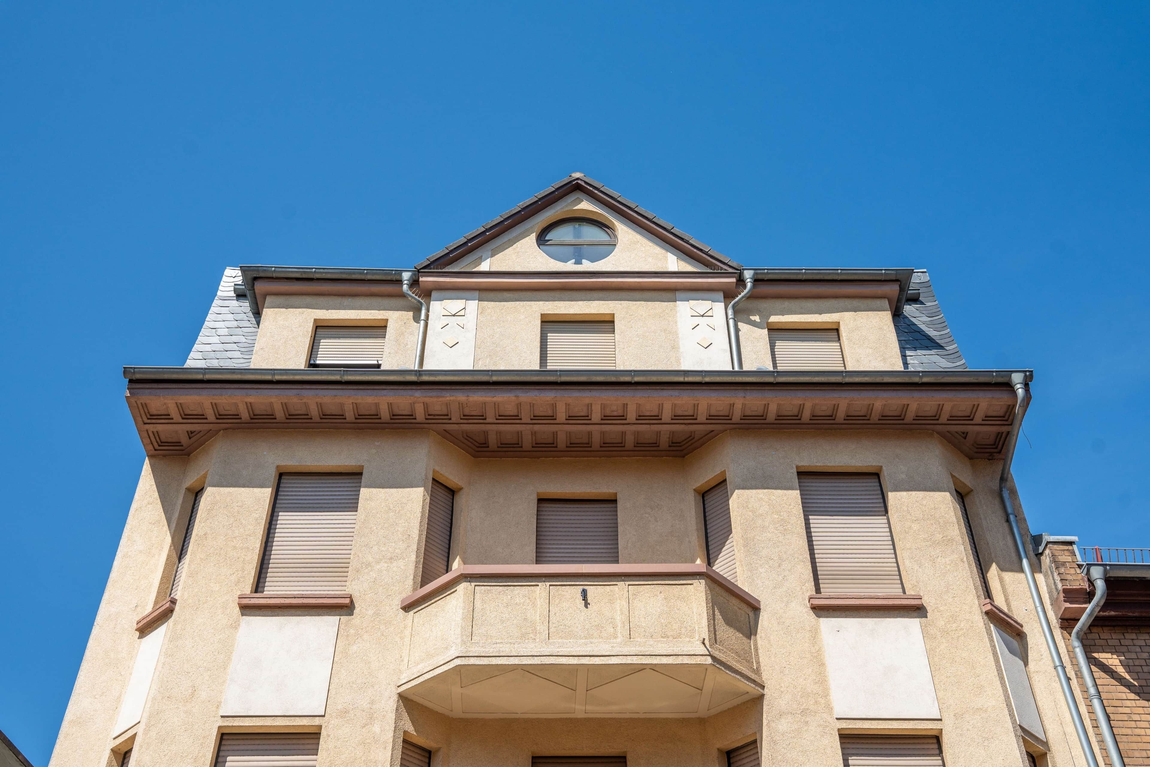 Un immeuble à plusieurs étages, doté d’une façade symétrique, d’un balcon central et d’un toit en pente.