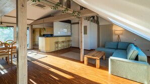 A spacious living area with a wooden ceiling, a sofa, a coffee table, and a kitchen area with a bar.