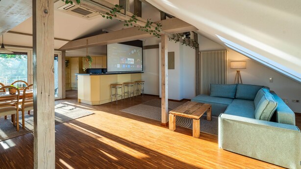 Ampla sala de estar com teto de madeira, sofá, mesa de centro e área de cozinha com balcão.