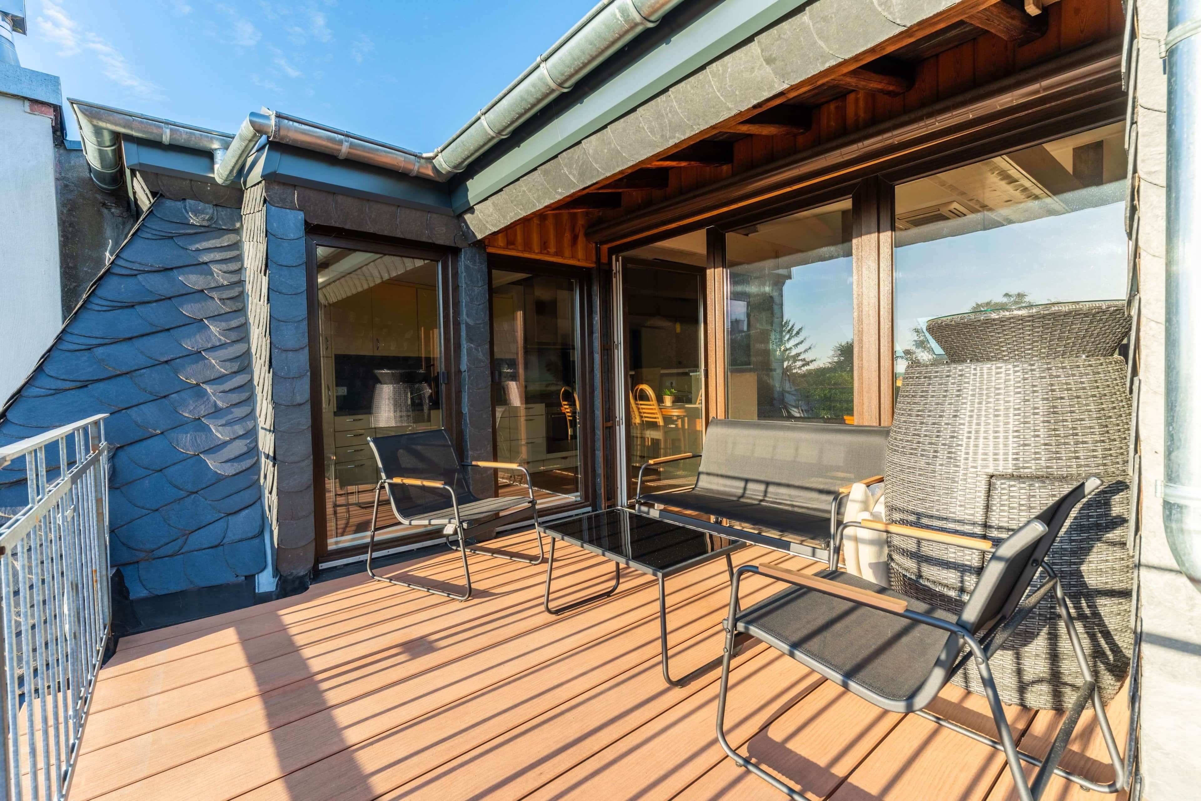 A wooden deck with outdoor furniture, a glass door entrance, and a view of the surrounding area.