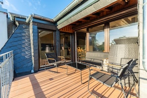 Une terrasse en bois avec mobilier d’extérieur, une porte-fenêtre et une vue sur les environs.