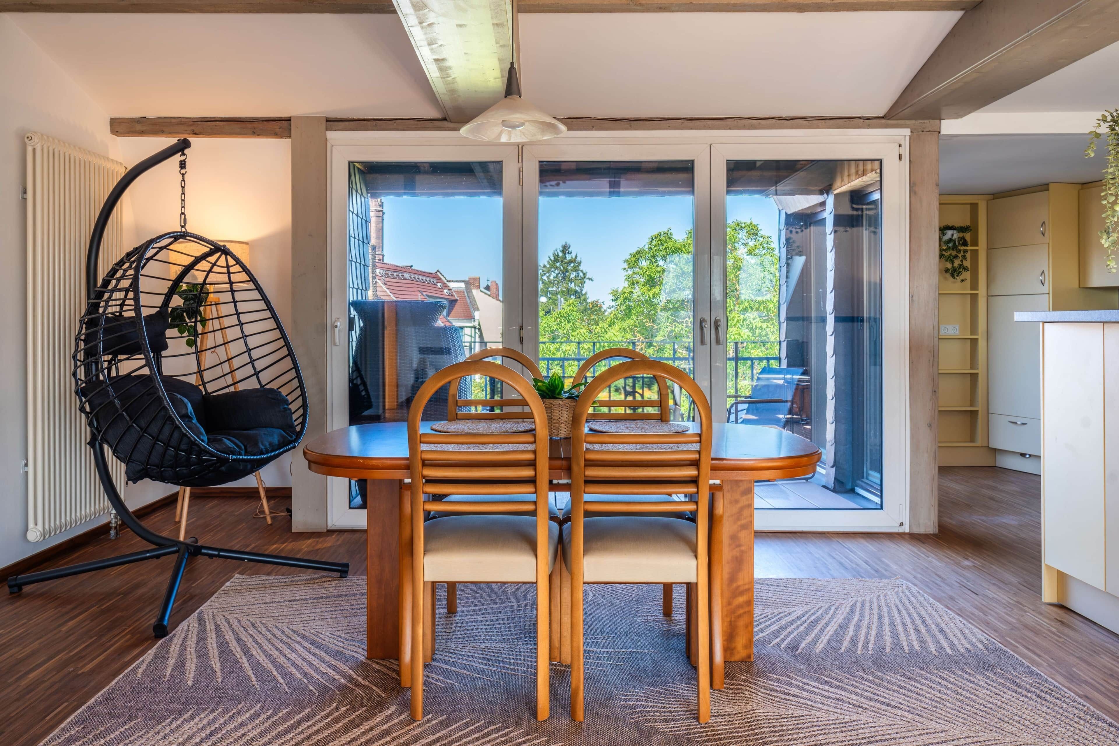 Un espace repas comprenant une table et des chaises, un fauteuil suspendu et une vue dégagée grâce à de grandes portes vitrées.