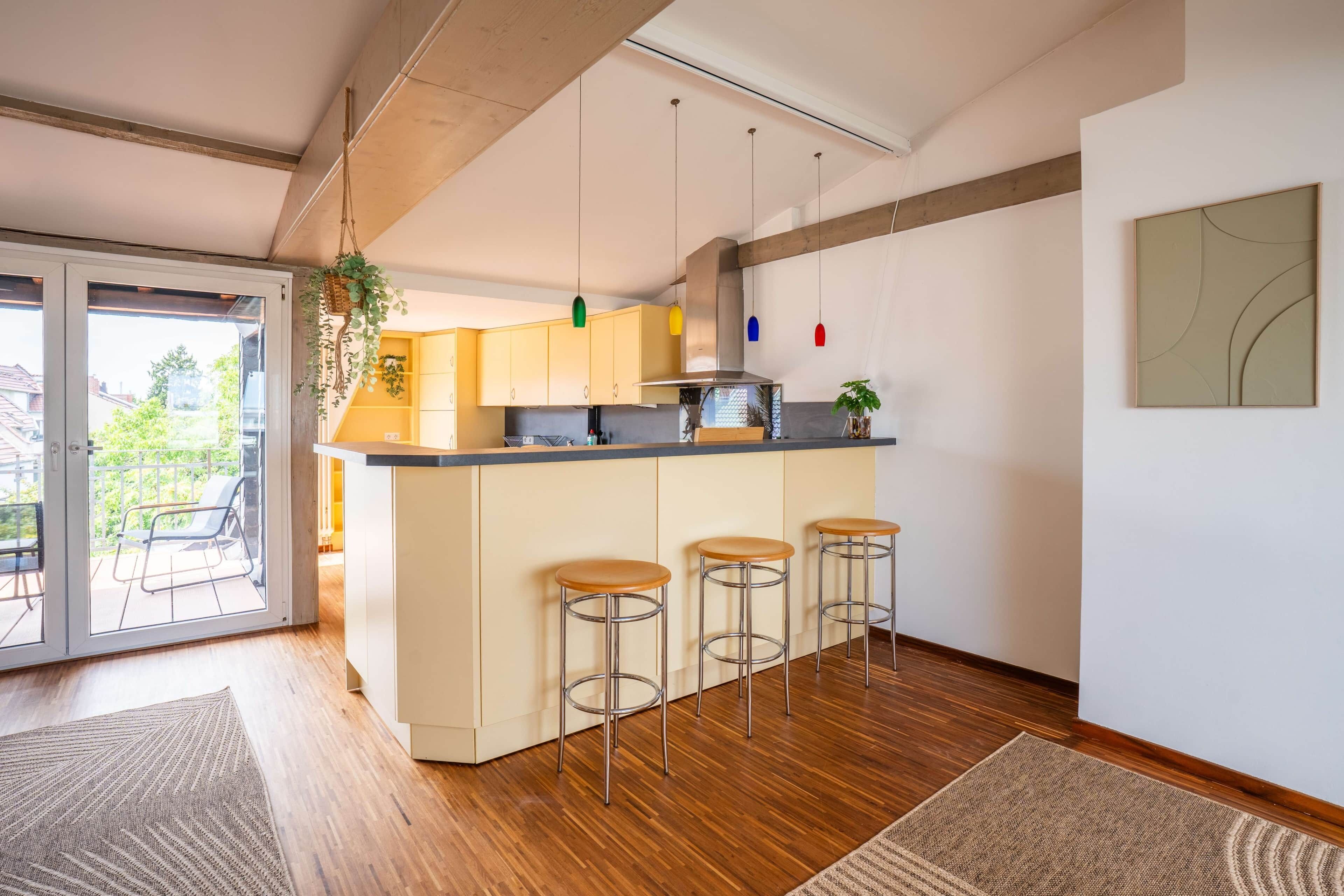 Une cuisine moderne dotée d’un îlot central, de tabourets de bar, de luminaires suspendus et donnant sur un espace extérieur grâce à une porte vitrée.