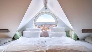 A bedroom with a large bed, a skylight, and a view of buildings outside.