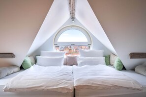 A bedroom with a large bed, a skylight, and a view of buildings outside.