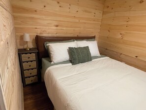 Een kamer met houten lambrisering, een bed, een nachtkastje en een lamp.