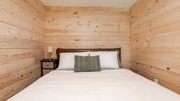 Une pièce avec un mur lambrissé en bois, un lit avec une literie blanche, une table de chevet avec une lampe et un coussin décoratif en tissu tissé.